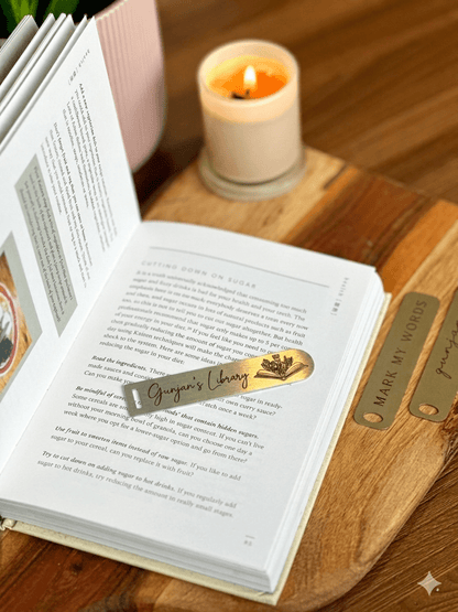 A close-up shot of an engraved gold-toned metal page marker strip resting across the pages of a novel