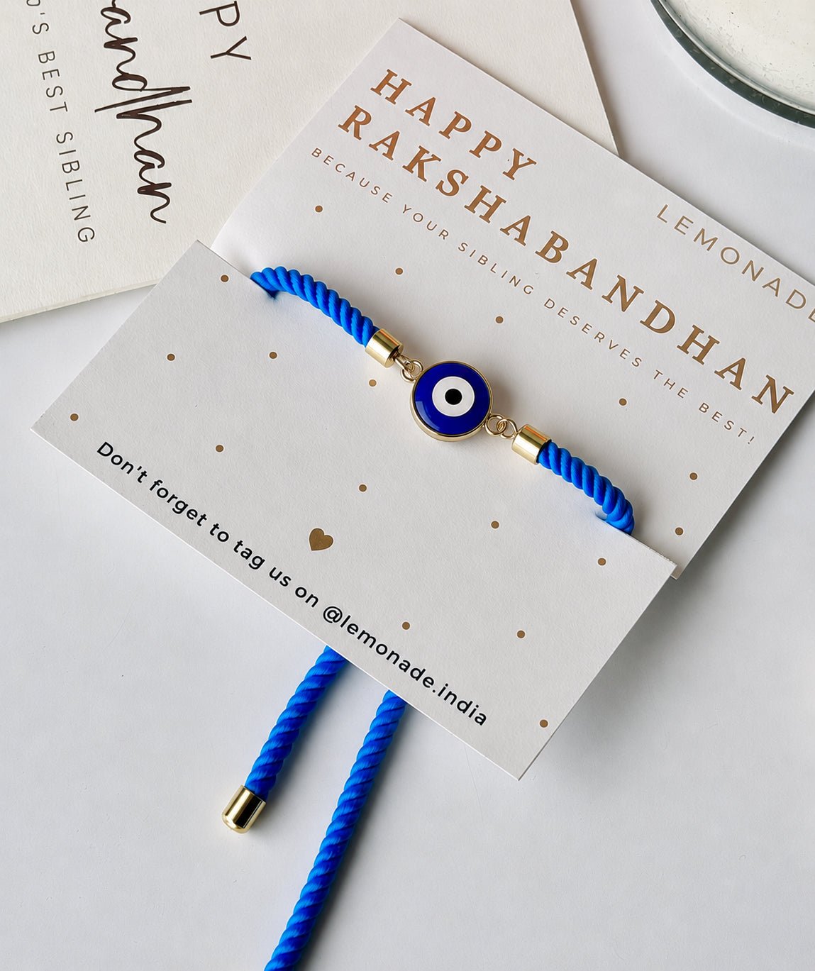 Mini Evil Eye Rakhi with a blue evil eye charm on a braided blue and white thread, handcrafted for Raksha Bandhan gifting
