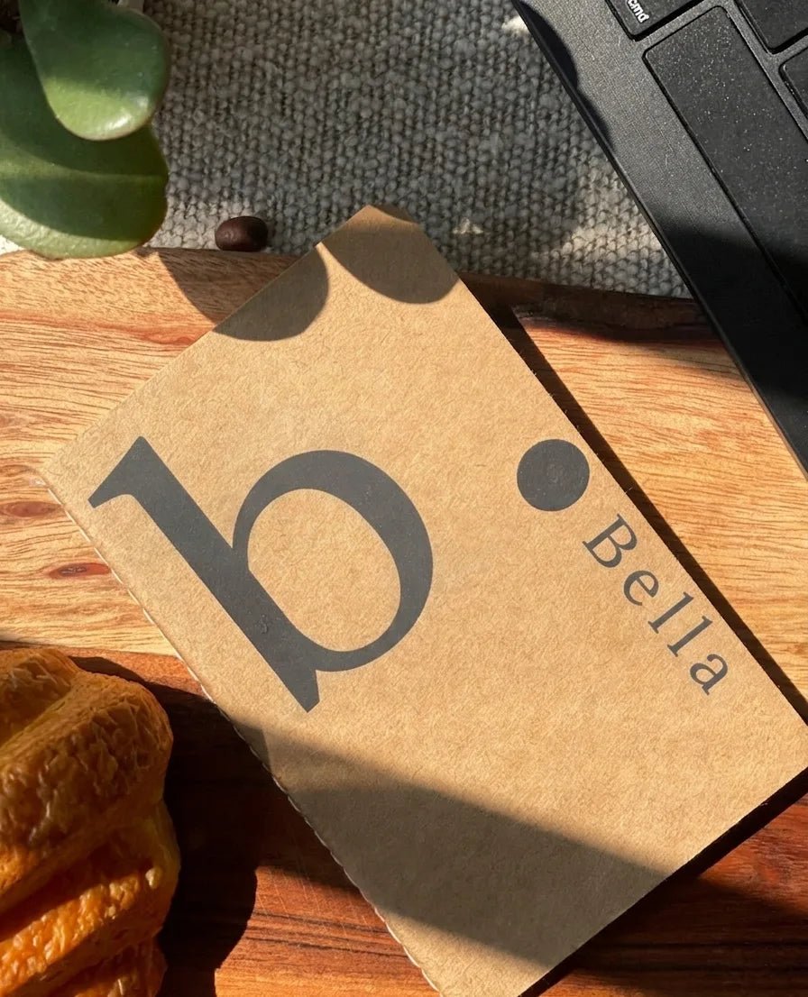 Personalized monogram mini kraft book with a bold black custom design on a natural brown paper cover, captured in an aesthetic flat lay setup under warm sunlight.